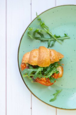 Tahta bir masada seramik tabakta roket salatası ve sebzeli kruvasan.