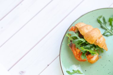 Tahta bir masada seramik tabakta roket salatası ve sebzeli kruvasan.