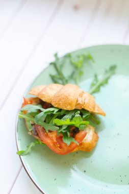 Tahta bir masada seramik tabakta roket salatası ve sebzeli kruvasan.