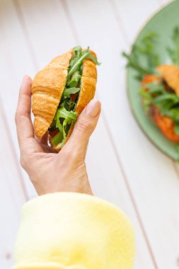 Elinde roka ve sebzeli kruvasan var.