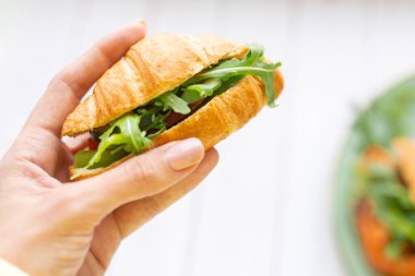 Elinde roka ve sebzeli kruvasan var.