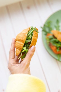 Elinde roka ve sebzeli kruvasan var.