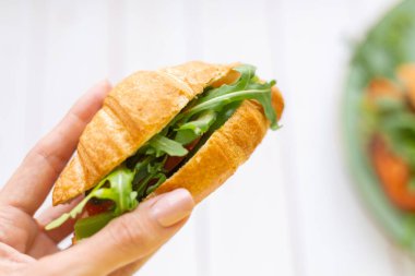 Elinde roka ve sebzeli kruvasan var.