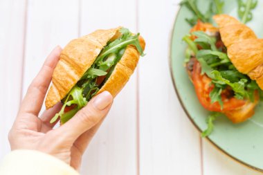 Elinde roka ve sebzeli kruvasan var.