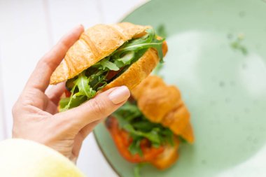 Elinde roka ve sebzeli kruvasan var.