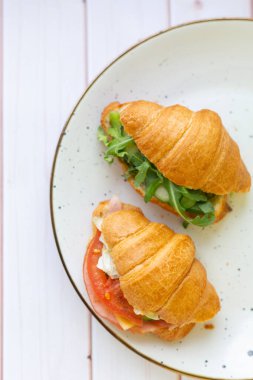 Tahta bir masada seramik bir tabakta roket salatası ve sebzeli iki coissant.