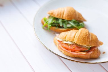 Tahta bir masada seramik bir tabakta roket salatası ve sebzeli iki coissant.