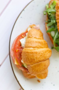 Tahta bir masada seramik bir tabakta roket salatası ve sebzeli iki coissant.