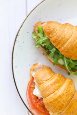 Tahta bir masada seramik bir tabakta roket salatası ve sebzeli iki coissant.