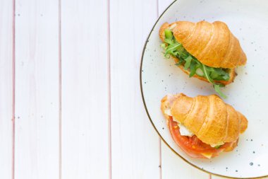 Tahta bir masada seramik bir tabakta roket salatası ve sebzeli iki coissant.