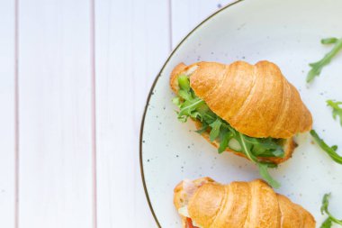 Tahta bir masada seramik bir tabakta roket salatası ve sebzeli iki coissant.