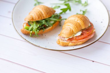 Tahta bir masada seramik bir tabakta roket salatası ve sebzeli iki coissant.