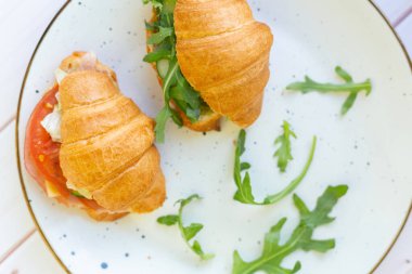 Tahta bir masada seramik bir tabakta roket salatası ve sebzeli iki coissant.