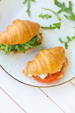 Tahta bir masada seramik bir tabakta roket salatası ve sebzeli iki coissant.