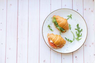 Tahta bir masada seramik bir tabakta roket salatası ve sebzeli iki coissant.