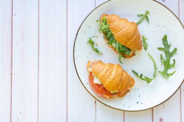 Tahta bir masada seramik bir tabakta roket salatası ve sebzeli iki coissant.
