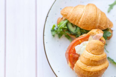 Tahta bir masada seramik bir tabakta roket salatası ve sebzeli iki coissant.