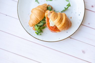 Tahta bir masada seramik bir tabakta roket salatası ve sebzeli iki coissant.