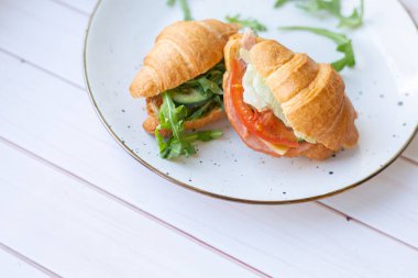 Tahta bir masada seramik bir tabakta roket salatası ve sebzeli iki coissant.