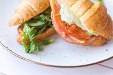 Tahta bir masada seramik bir tabakta roket salatası ve sebzeli iki coissant.