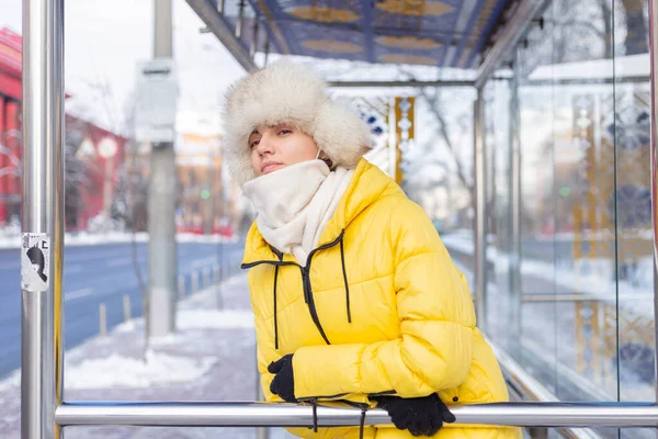 Woman in winter clothes on a cold day waiting for a bus at a bus stop