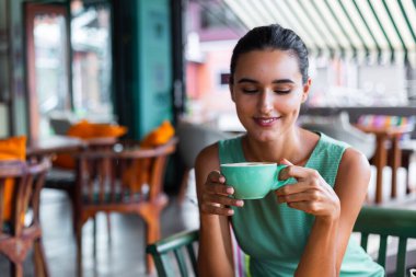 Cute elegant calm happy woman in green summer dress sits with coffee in cafe enjoying morning