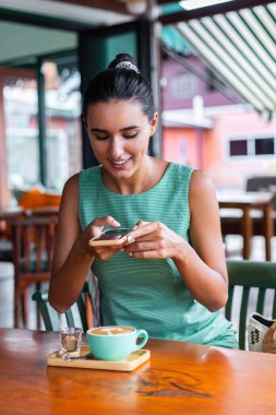 Tanned pretty woman smiling and take photo of coffee in cafe