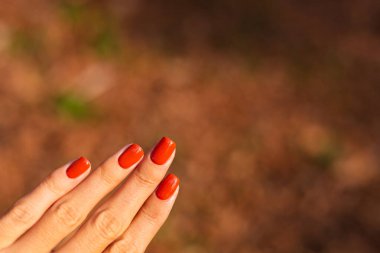 Kadınların parktaki ellerini yakın çekimde turuncu manikür, sonbahar havası..