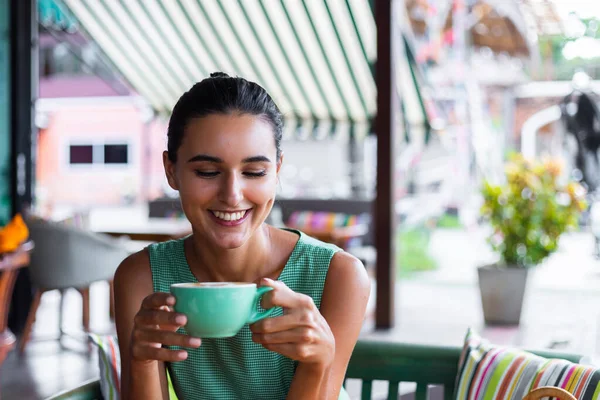 Cute elegant calm happy woman in green summer dress sits with coffee in cafe enjoying morning