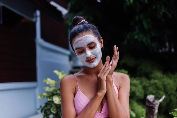 Outdoor portrait of tanned skin calm pretty caucasian woman in bikini at spa with white peeling mask on face