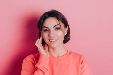Güzel, gülümseyen esmer kadın modelinin portresi. Günlük şeftali rengi süveter, parlak makyaj ve pembe dudaklar.