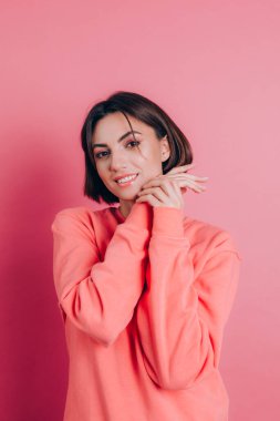 Güzel, gülümseyen esmer kadın modelinin portresi. Günlük şeftali rengi süveter, parlak makyaj ve pembe dudaklar.