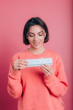 Mutlu gülümseyen kızın portresi pembe arka planda izole edilmiş hediye kutusunu açıyor.