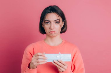 Hüsrana uğramış bir kızın portresi pembe arka planda izole edilmiş hediye kutusunu açıyor.