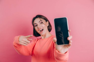 Şu cep telefonuna bak! Mutlu kadın işaretleri boş ekrana işaret ediyor, modern aletler gösteriyor, mutlu ve şaşırmış duygular..