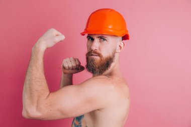 Pembe arka planda miğferli güçlü dövmeli üstsüz Avrupalı adam.