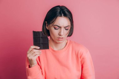 Karın ağrısı olan, pembe arka planda çikolatalı ve parlak makyajlı güzel, üzgün bir kadın.