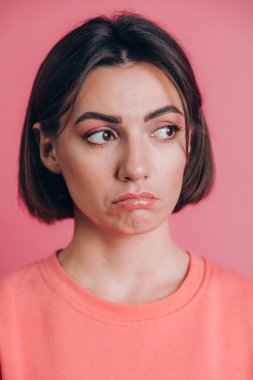 Pembe arka planda parlak makyajlı üzgün genç bir kadının portresi.