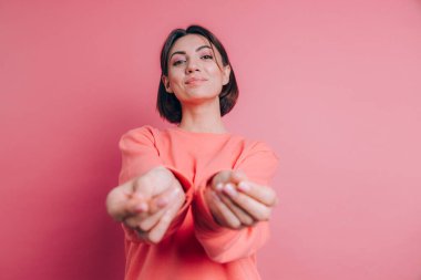 Gülümseyen genç esmer kadın, 20 'li yaşlarda, gündelik ayakta duran parmaklarını ovuşturuyor, nakit jest yapıyor, para istiyor, pembe arka plan.