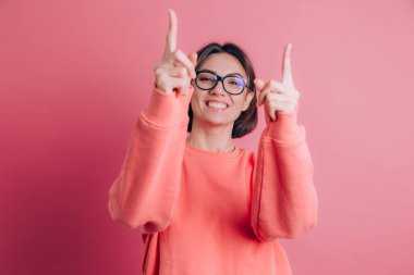 Arka planda süveter giyen kadın seni ve kamerayı parmaklarıyla gösteriyor, gülümsüyor pozitif ve neşeli.