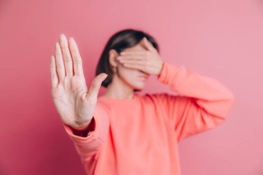 Arka planda sıradan bir süveter giyen kadın elleriyle gözlerini kapatıyor ve üzgün ve korku ifadeleriyle jest yapıyor.