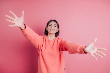 Arka planda sıradan bir süveter giyen kadın kameraya sarılmak için gülümseyerek bakıyor.