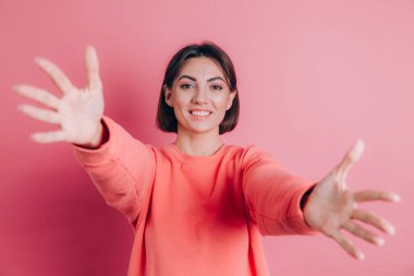 Arka planda sıradan bir süveter giyen kadın kameraya sarılmak için gülümseyerek bakıyor.