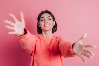 Arka planda sıradan bir süveter giyen kadın kameraya sarılmak için gülümseyerek bakıyor.