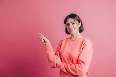 Arka planda süveter giyen, gülümseyen ve kameraya bakan bir kadın. İşaret parmağıyla solu göster.