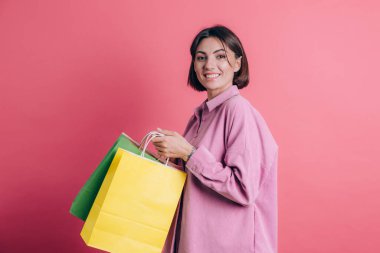 Arka planda rahat süveter giyen bir kadın renkli çantalarla alışverişin keyfini çıkarıyor.