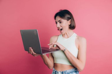 Pembe arka plandaki kadınlar çenelerini açık tutarlar dizüstü bilgisayarlarını tutarlar