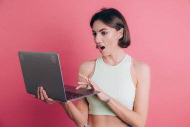 Pembe arka plandaki kadınlar çenelerini açık tutarlar dizüstü bilgisayarlarını tutarlar