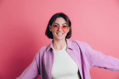 Genç, sevimli kadınlar pembe arka planda güneş gözlüğü takıyor hareketli, hareketli, dans eden zıplamalar yapıyor.