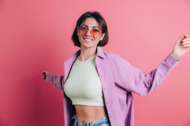 Genç, sevimli kadınlar pembe arka planda güneş gözlüğü takıyor hareketli, hareketli, dans eden zıplamalar yapıyor.